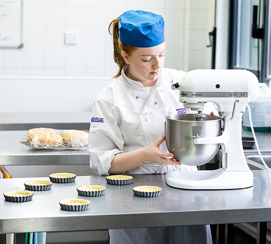 Hospitality student pouring cake mix into the mixer