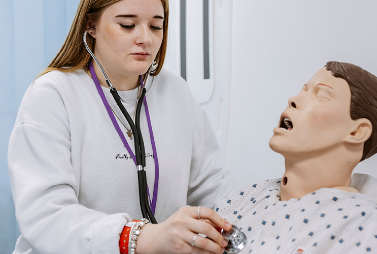 Female student practicing using stethoscope on dummy
