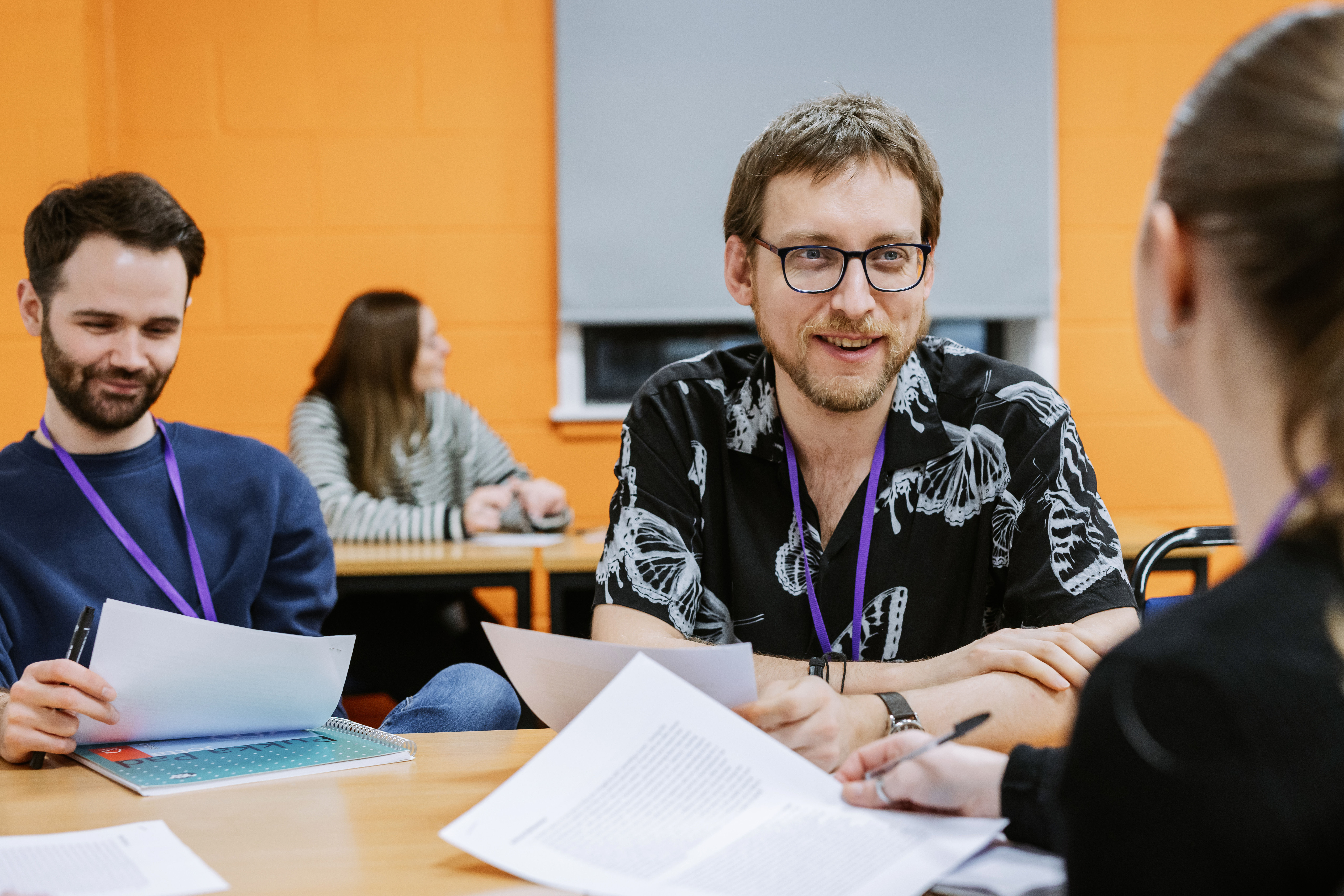 Male student sat smiling at table with paper