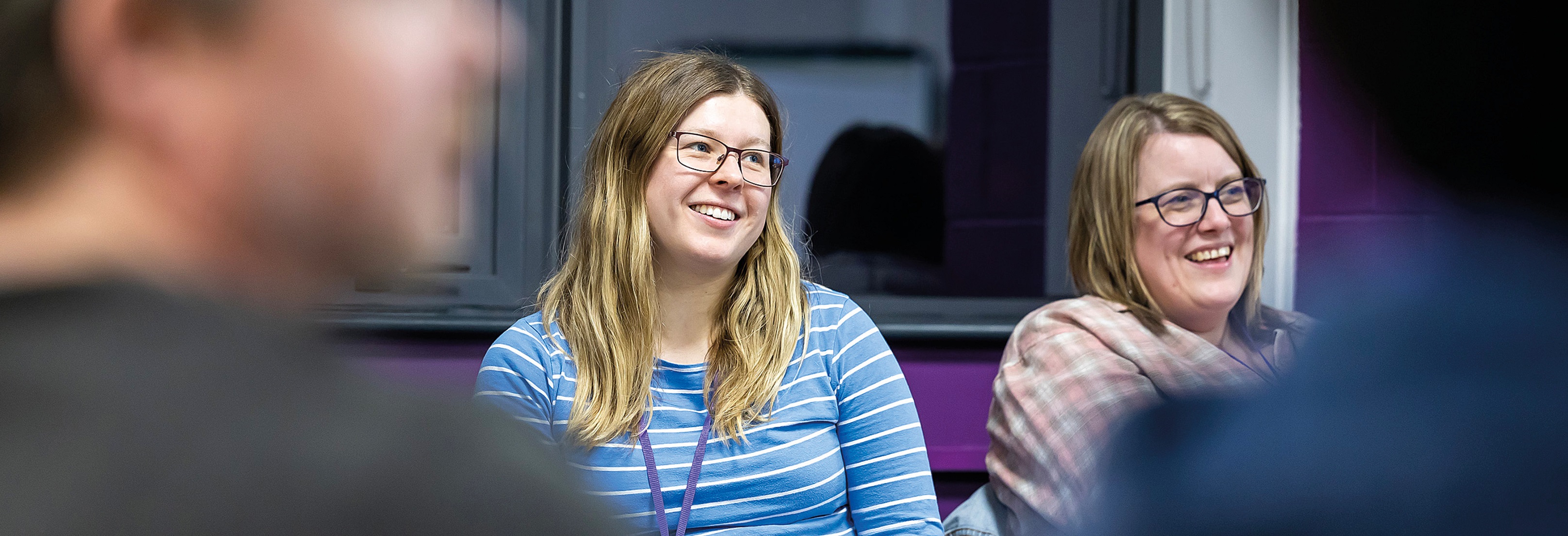 Adult Learners Sat In Group Smiling Towards Teacher